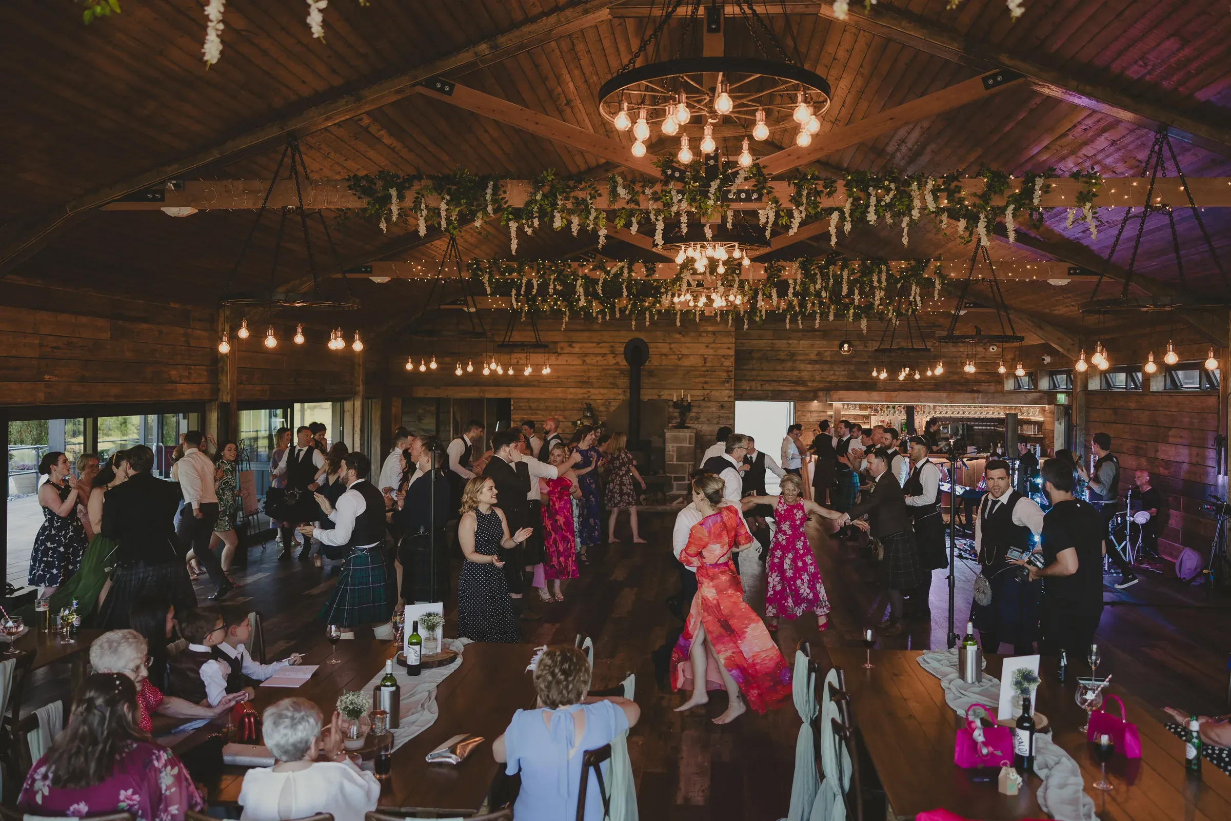 A lively scene of wedding guests dancing and enjoying themselves inside the rustic barn at Glenclova.