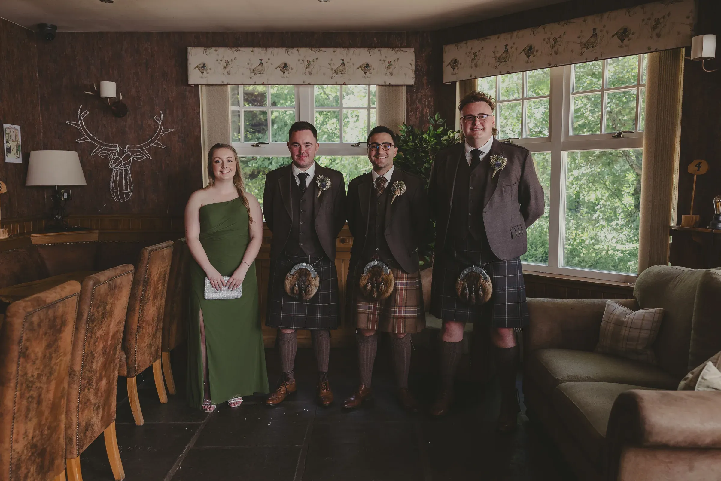 A happy group of groomsmen and a bridesmaid pose together inside one of the Glenclova lodges during Blair and Beth's wedding.