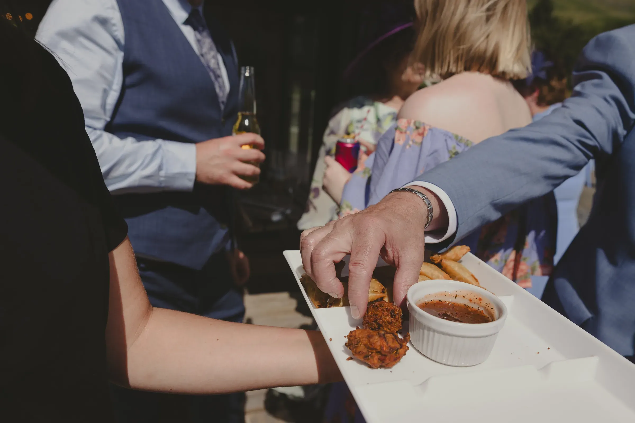 A guest reaches for a piece of buffet-style food served on a platter during a wedding reception.