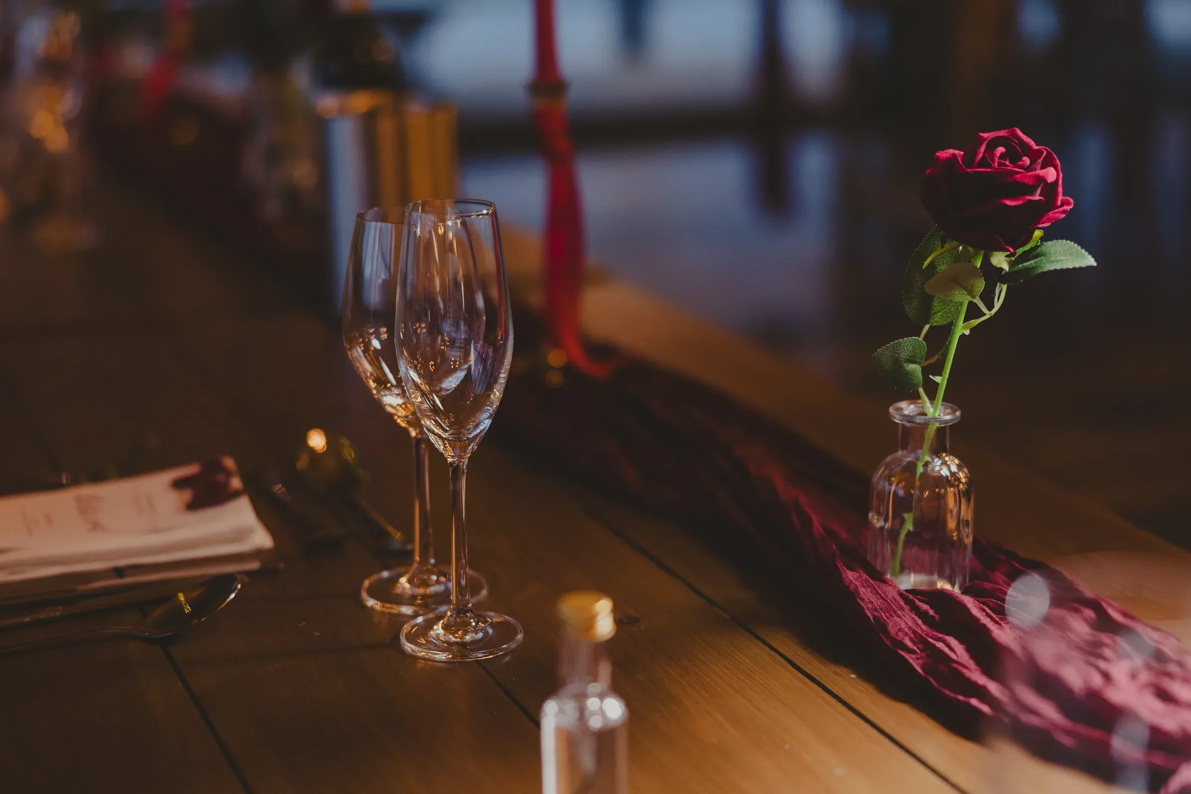 A beautifully staged table setting inside the barn featuring wine glasses and a single red rose.