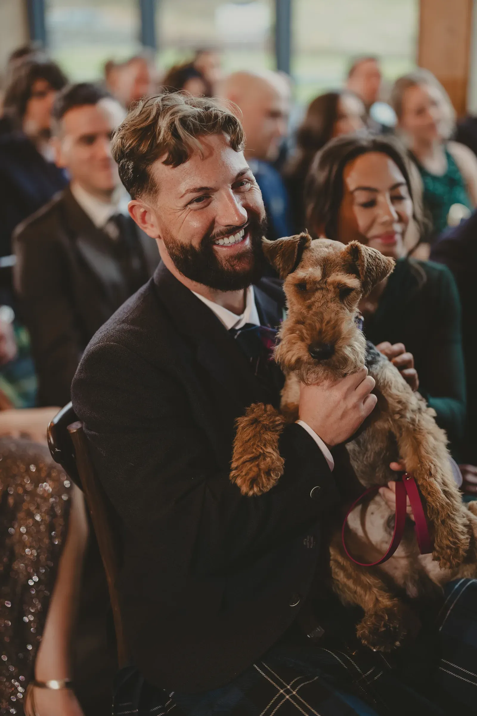 A groomsman holds a dog while smiling during a wedding ceremony at Glenclova.