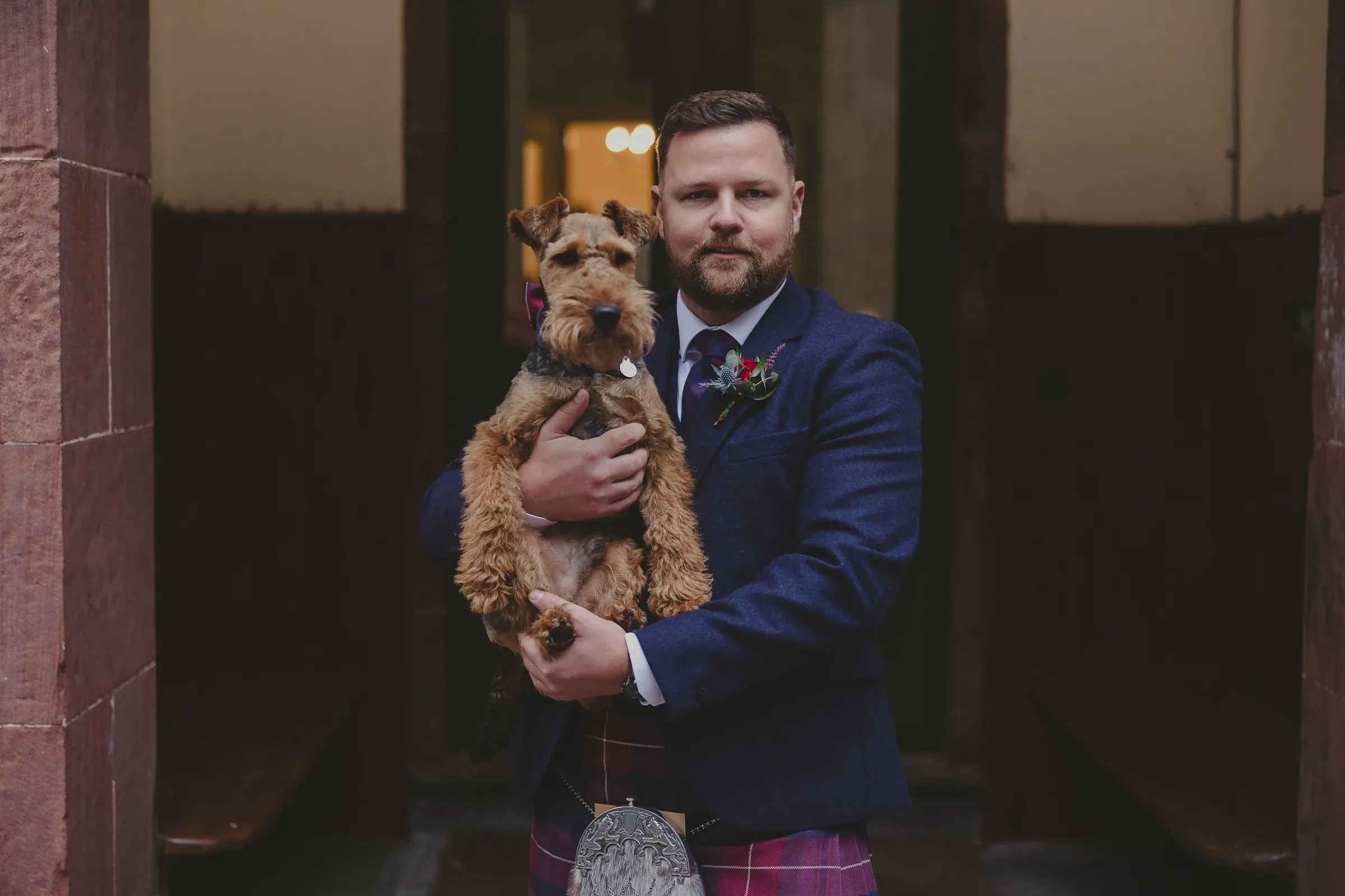 Kevin holds his dog, who is wearing a matching tartan accessory, outside the venue.