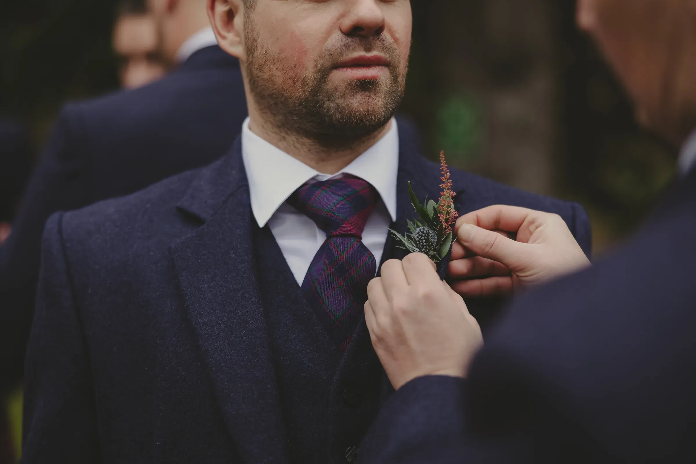 An up-close staging shot of a boutonniere being pinned onto a man's suit jacket.