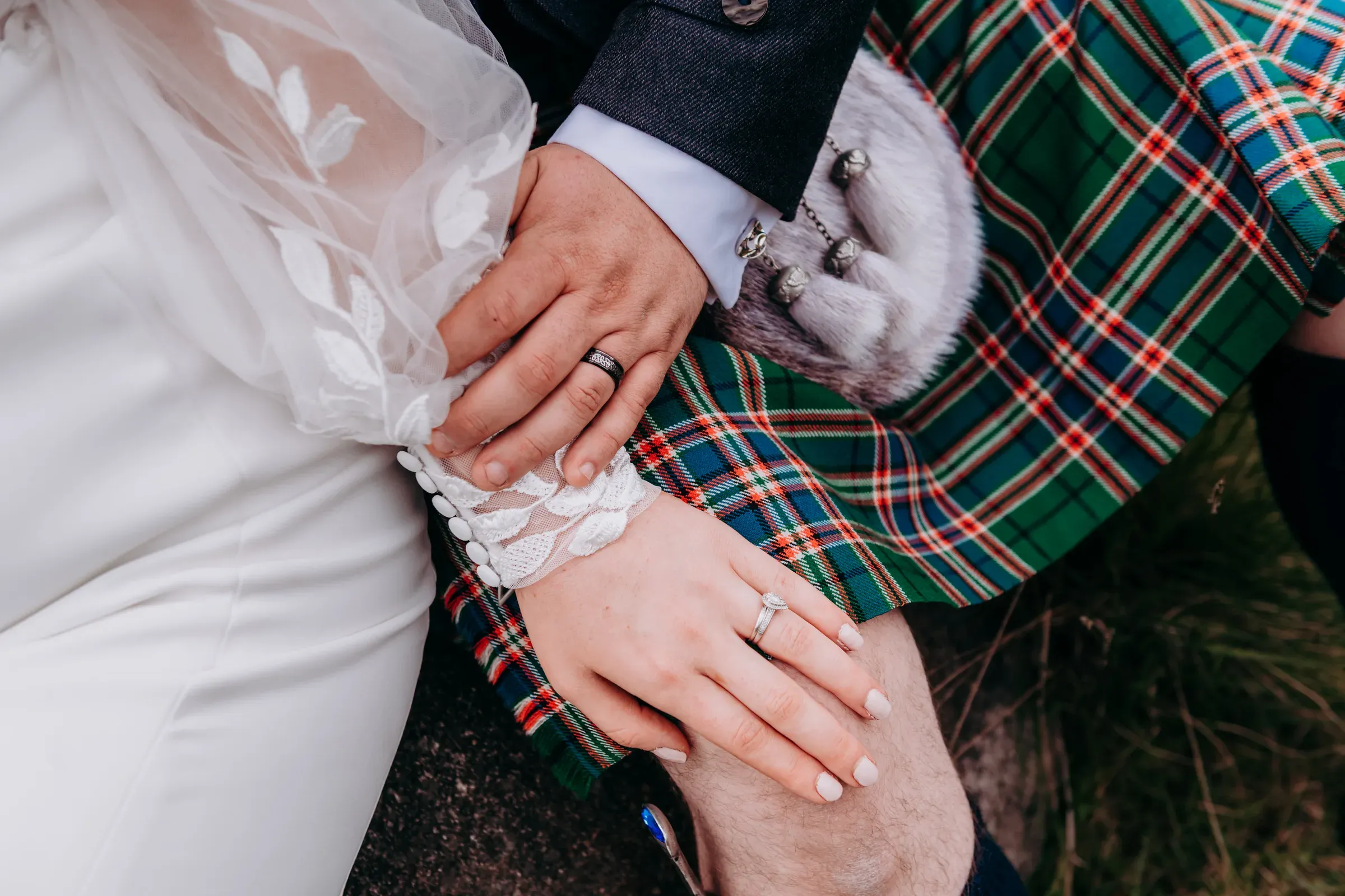 A close-up staging shot of Sam and Cam showing their wedding rings and the groom's kilt.