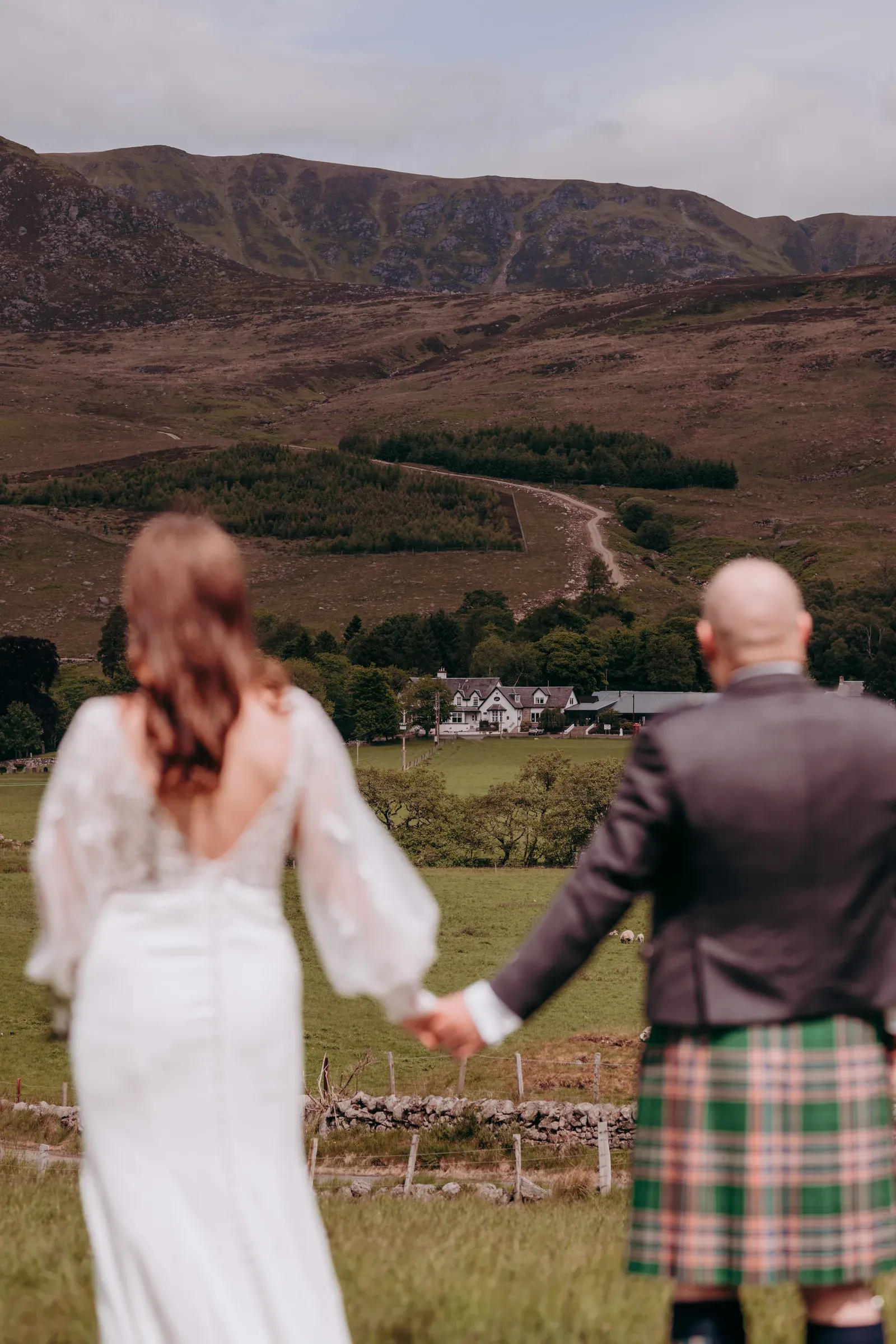 Sam and Cam hold hands in the foreground, looking out over the Glenclova hotel, lodges, and the surrounding glen.