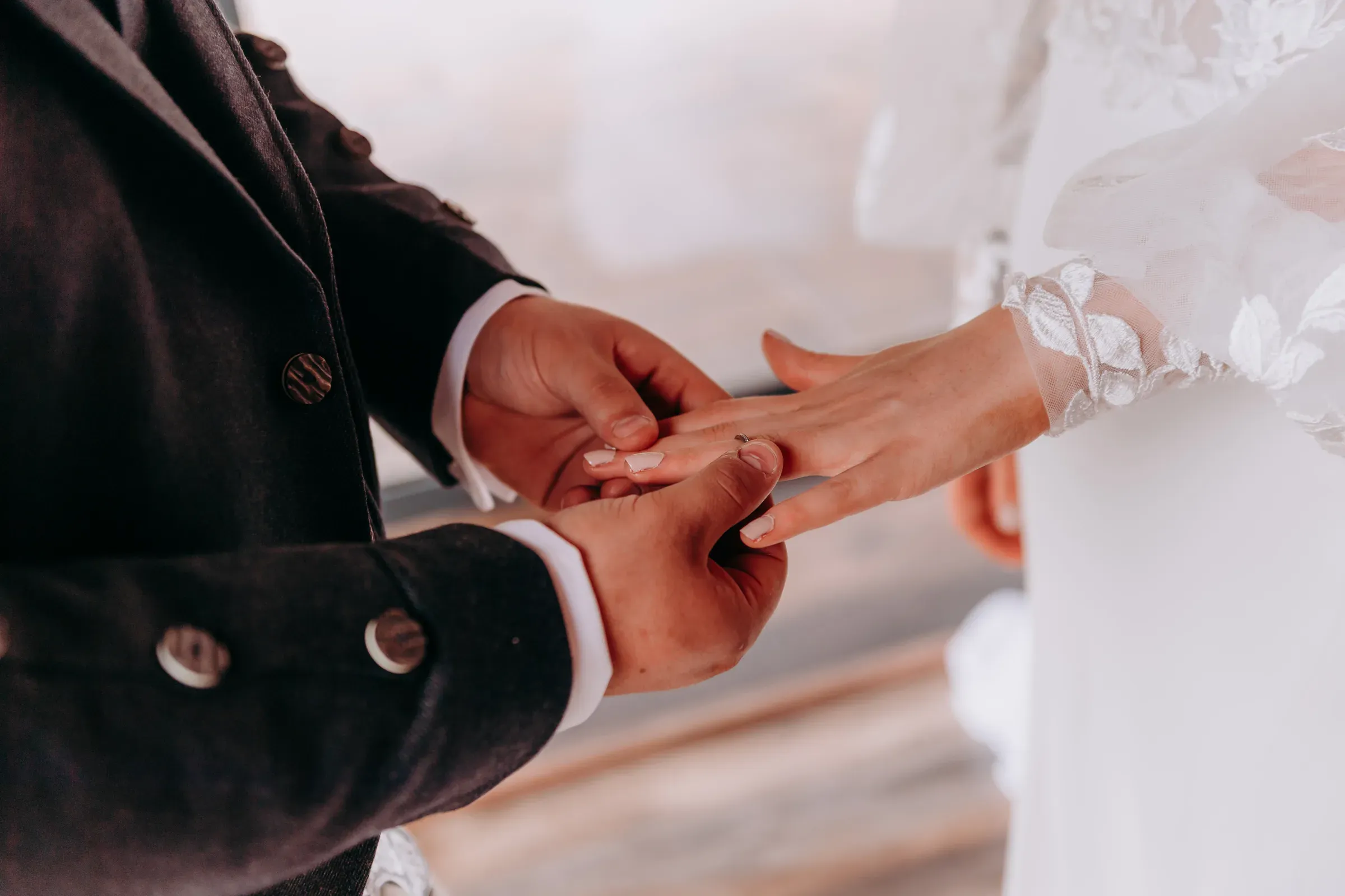 A close-up staging shot of Cam placing a wedding ring onto the finger of the bride, Sam.