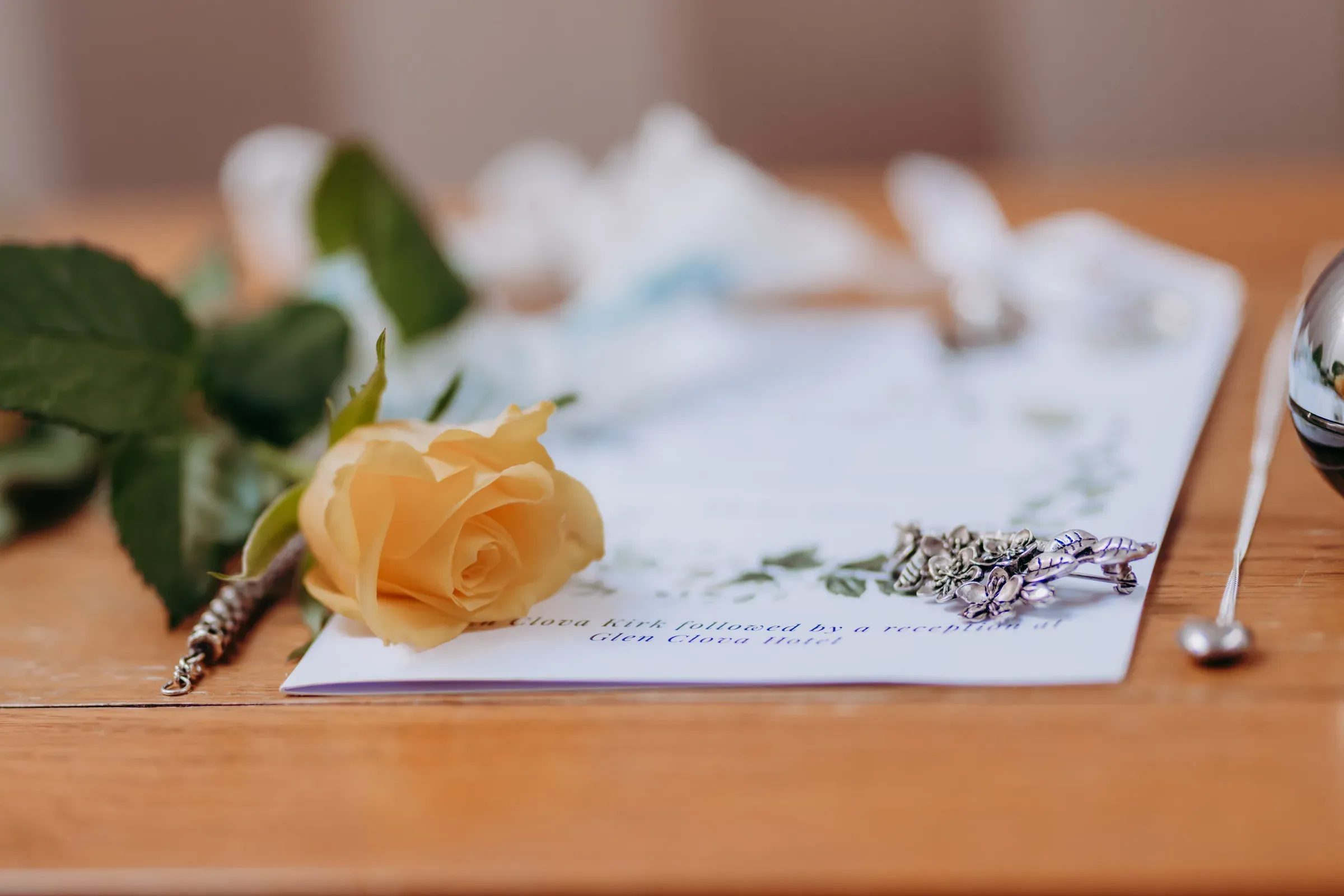 A soft-focus staging shot featuring a single yellow rose resting on wedding stationery.