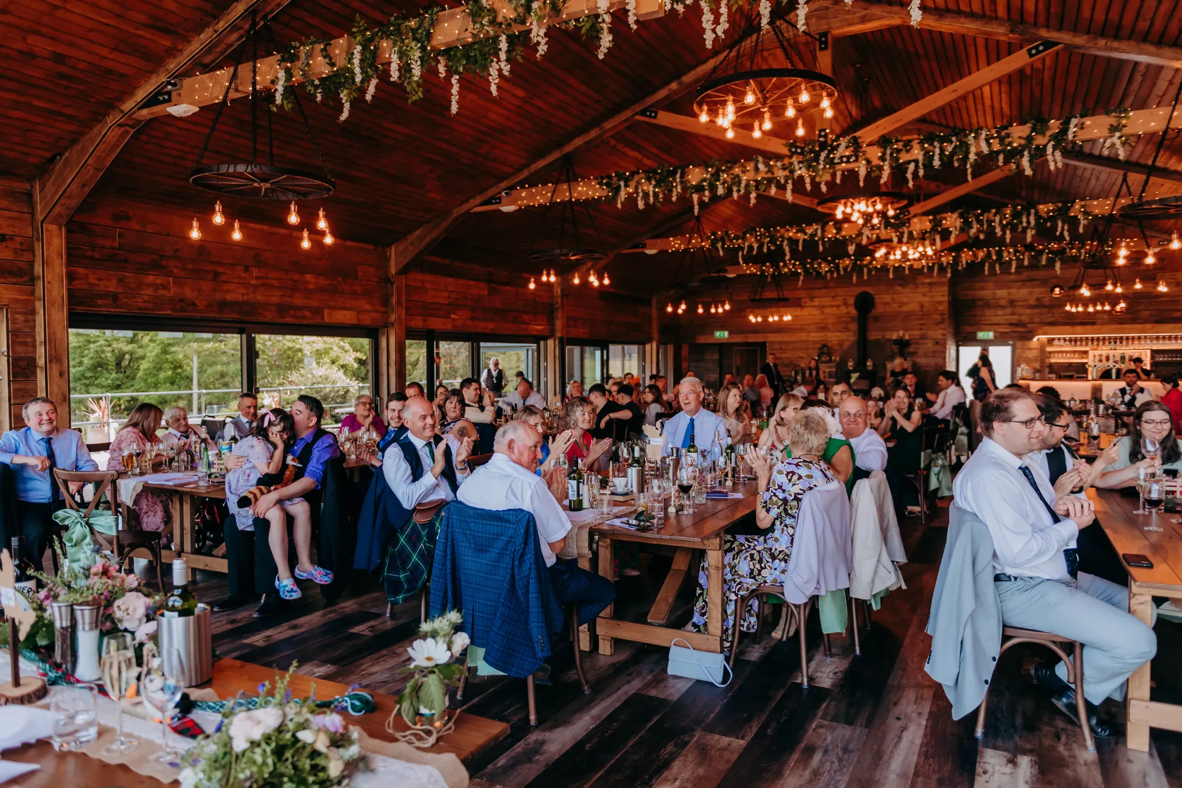 A bright and cosy barn reception filled with wedding guests celebrating during Heather and Louis's wedding.