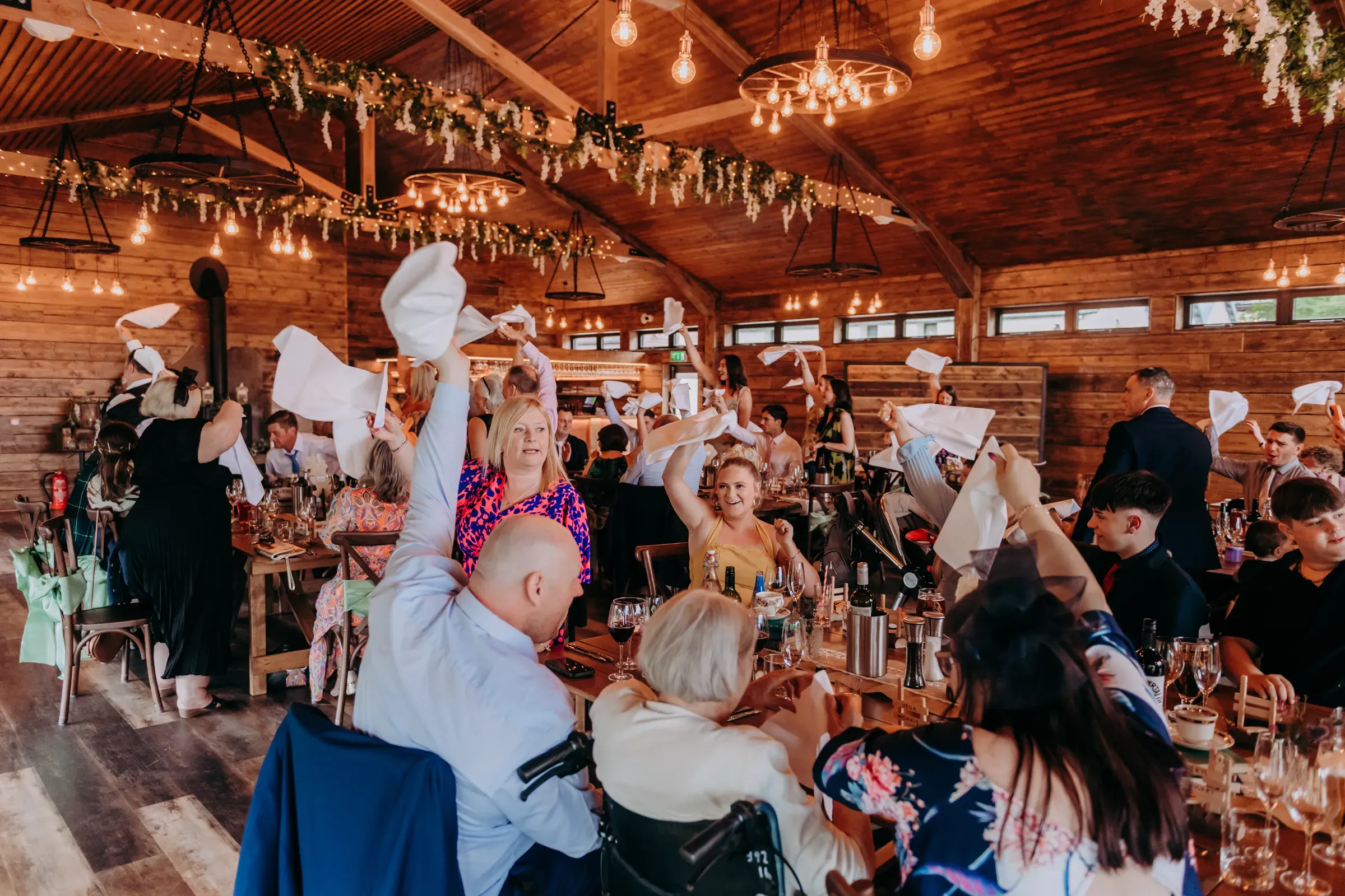 Wedding guests celebrate during the dinner reception by waving their napkins inside the barn at Glen Clova.