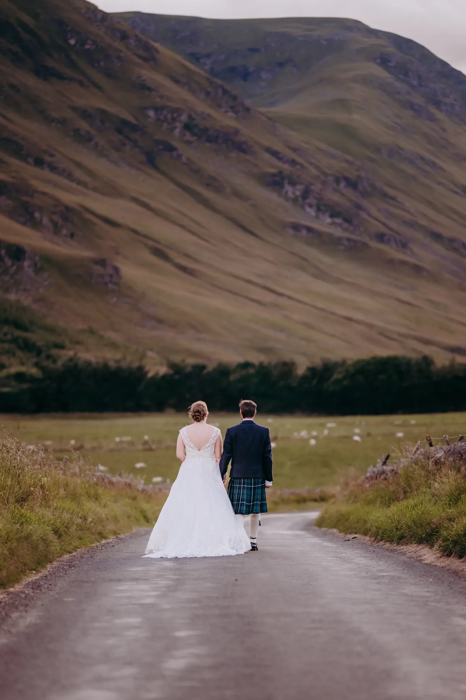 Newly married couple Heather and Louis walk hand-in-hand along a road leading into the Scottish Highland glen.