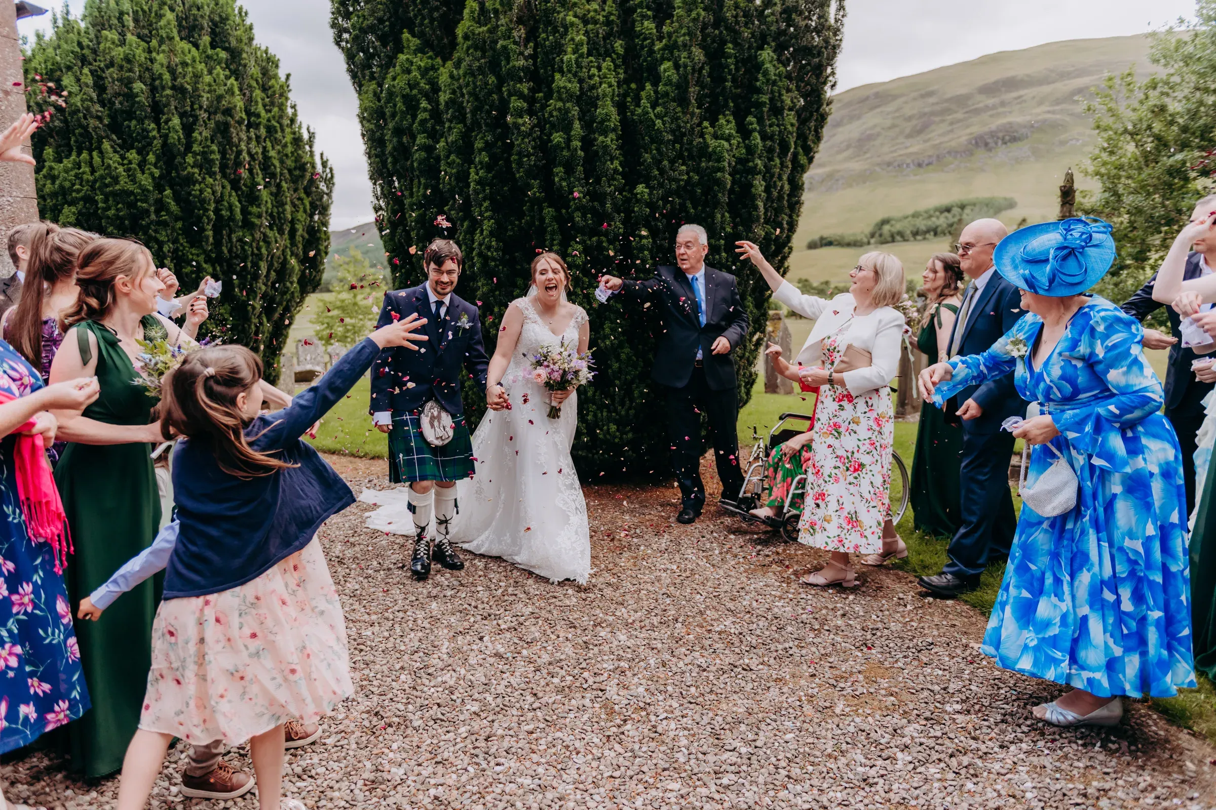 Heather and Louis walk out after their ceremony looking excited and happy while guests throw confetti.