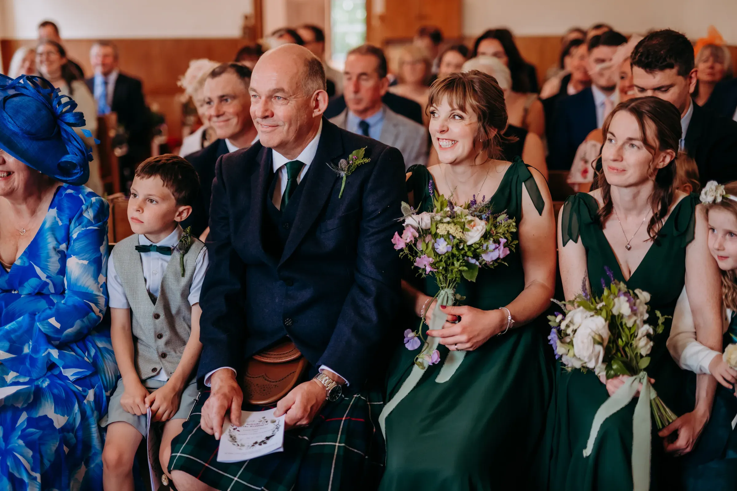 Wedding guests sit together inside the Kirk, looking happy and enjoying the ceremony.