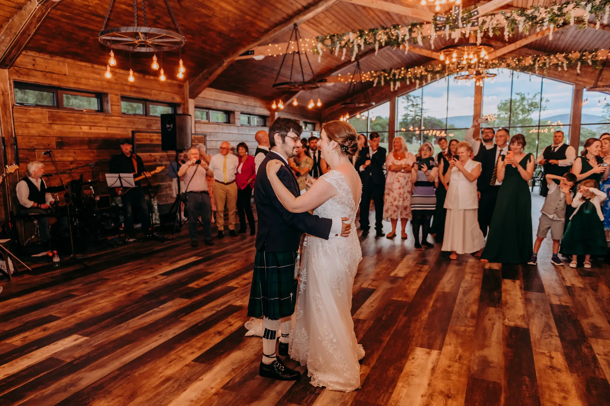The bride and groom share their first dance in the barn surrounded by wedding guests.