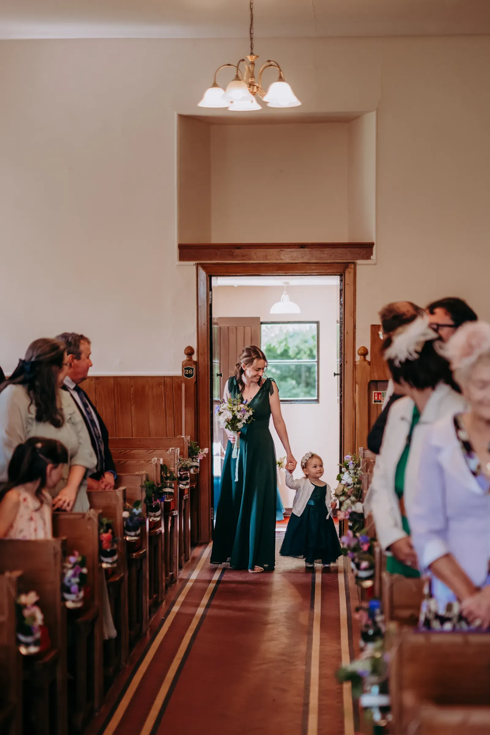 A bridesmaid and a young child walk down the aisle together during a wedding ceremony.