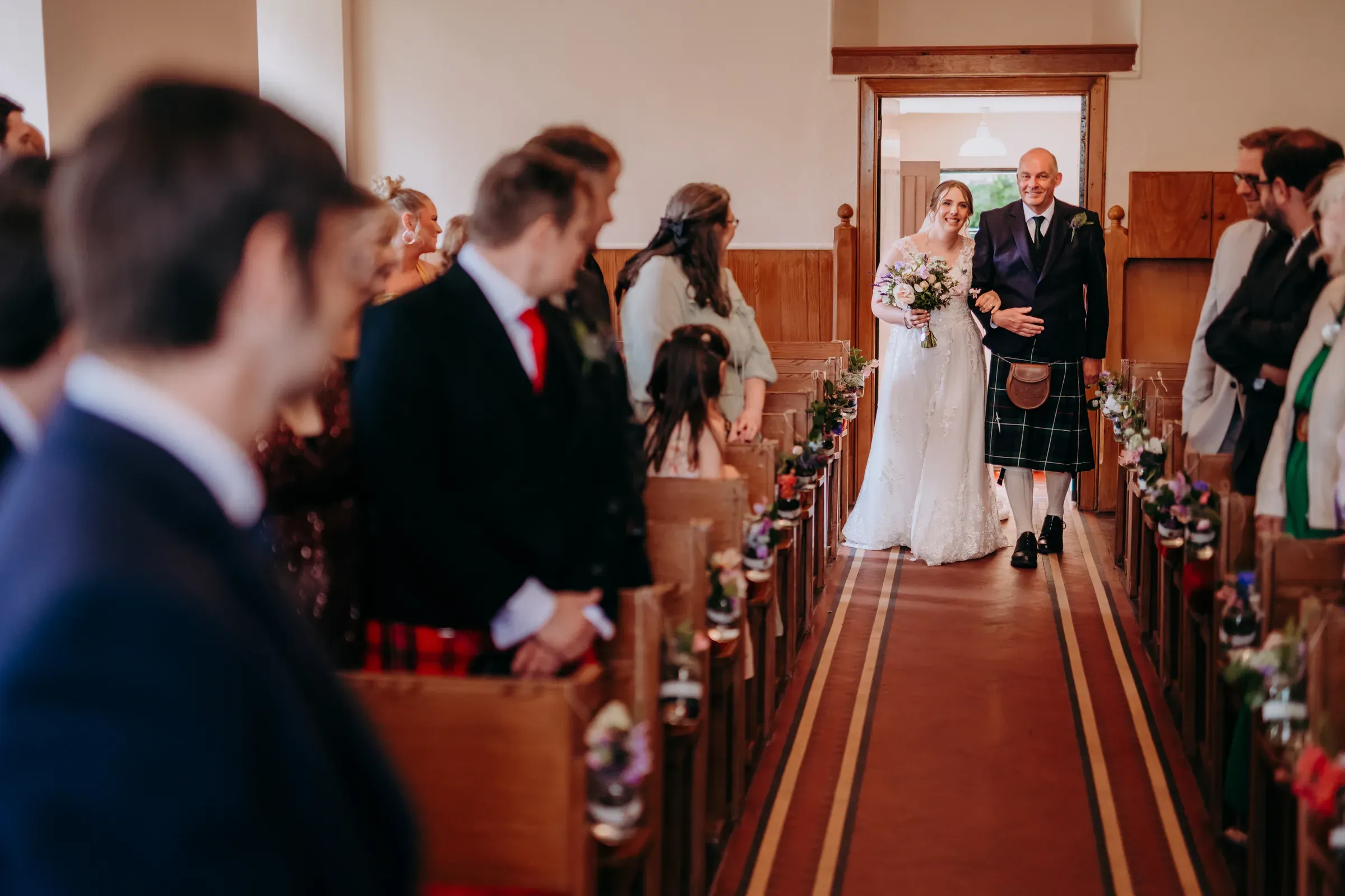 A bride is walked down the aisle of the kirk by her father during a wedding ceremony.
