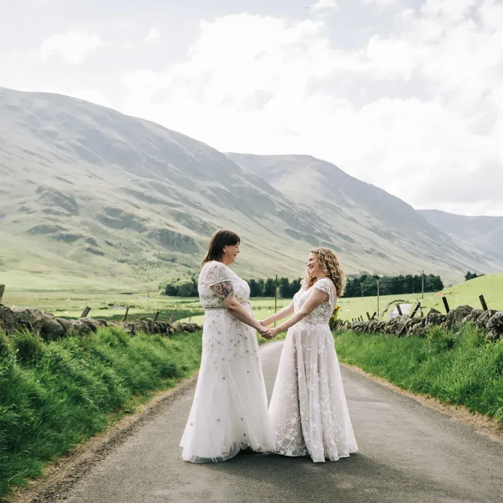 A happy wedding couple holding hands on a road set against the scenic backdrop of the glen.