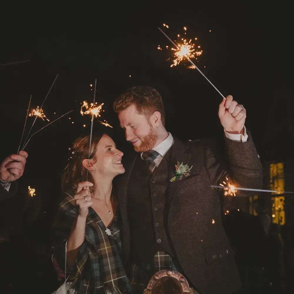 A happy wedding couple celebrates with sparklers at night.