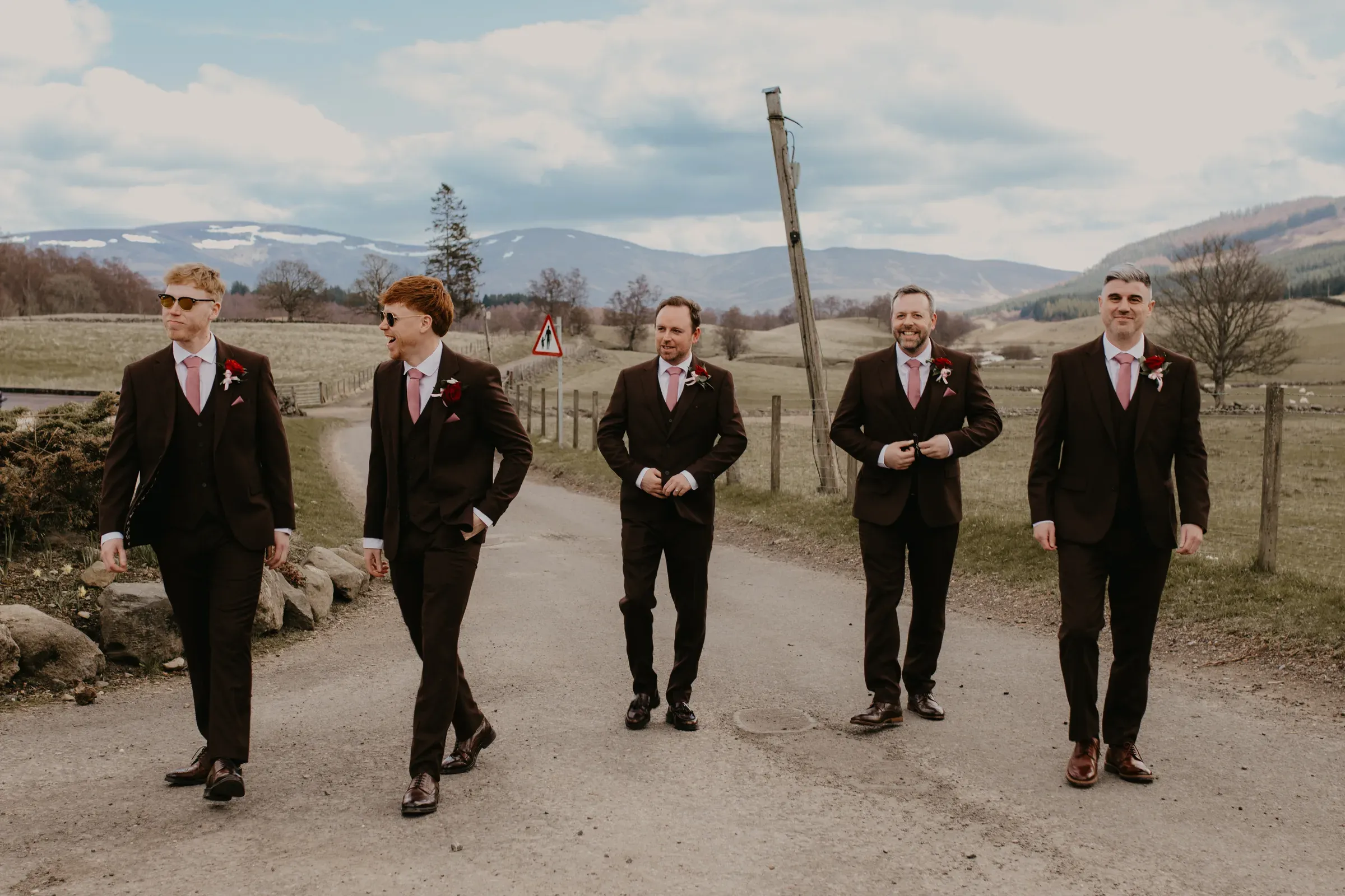 Ryan and his groomsmen walk along a path outside with the scenic glen in the background.