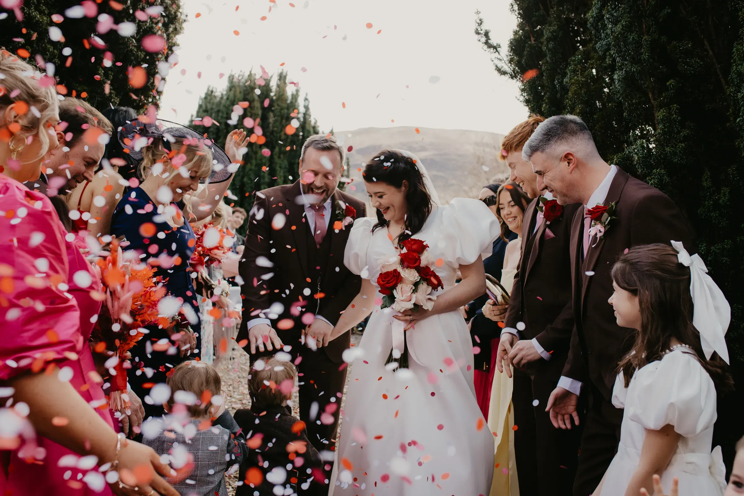 Meg and Ryan walk through a shower of confetti surrounded by happy wedding guests outside the ceremony area.