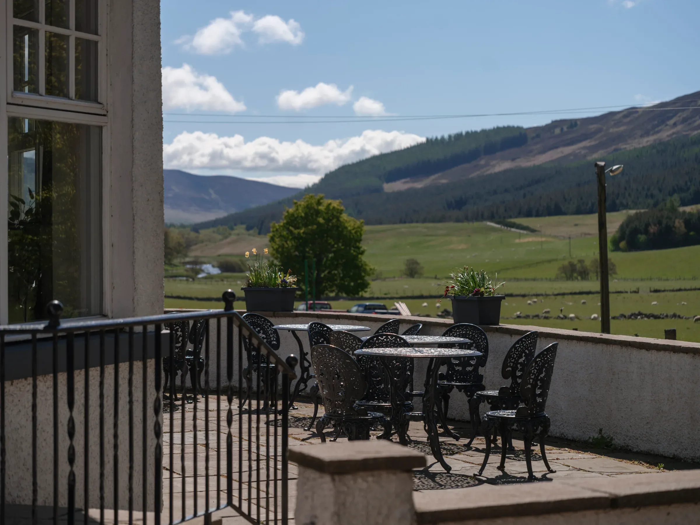 An outdoor seating area featuring metal tables and chairs with scenic views over the Scottish glen.