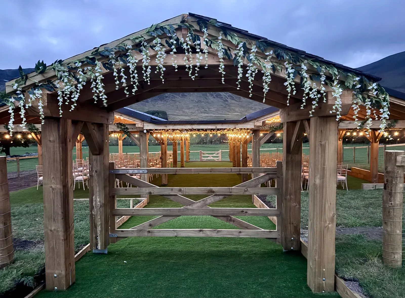 A view of the outdoor meadow wedding structure decorated with hanging flowers and fairy lights.