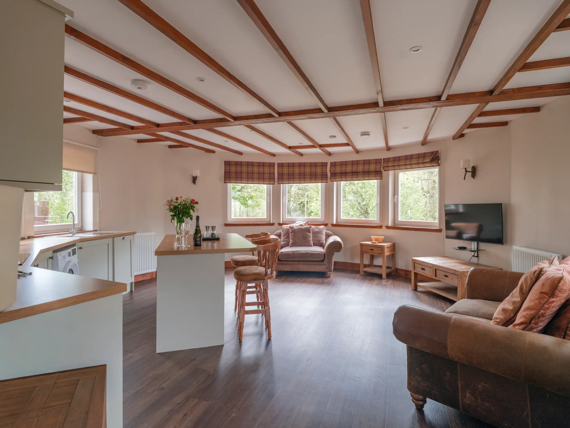 A full view of the interior of the Old Mill Lodge, featuring an open-plan kitchen and living area with wooden ceiling beams.
