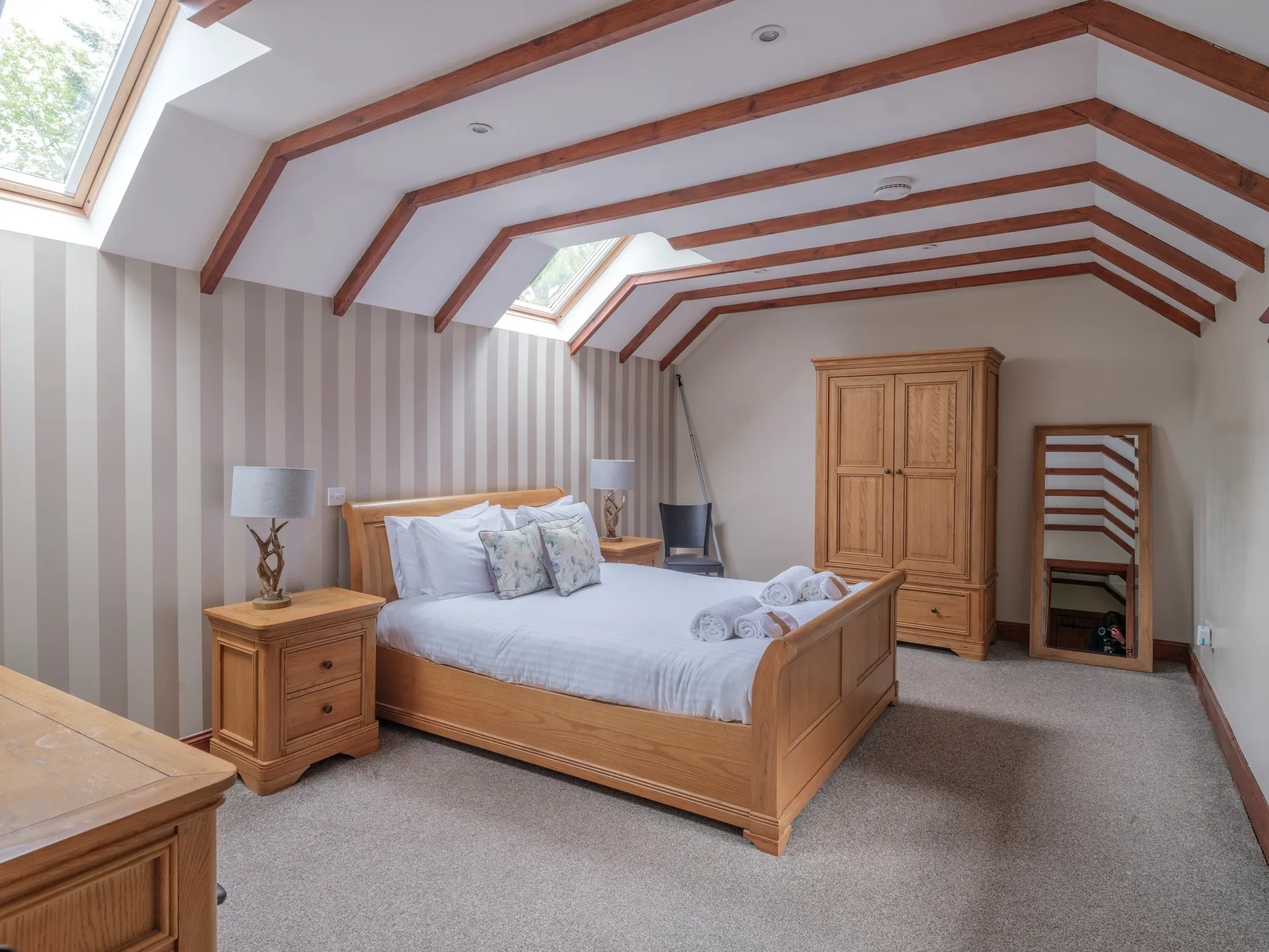A bright and spacious lodge bedroom featuring a wooden bed frame, exposed ceiling beams, and skylight windows.