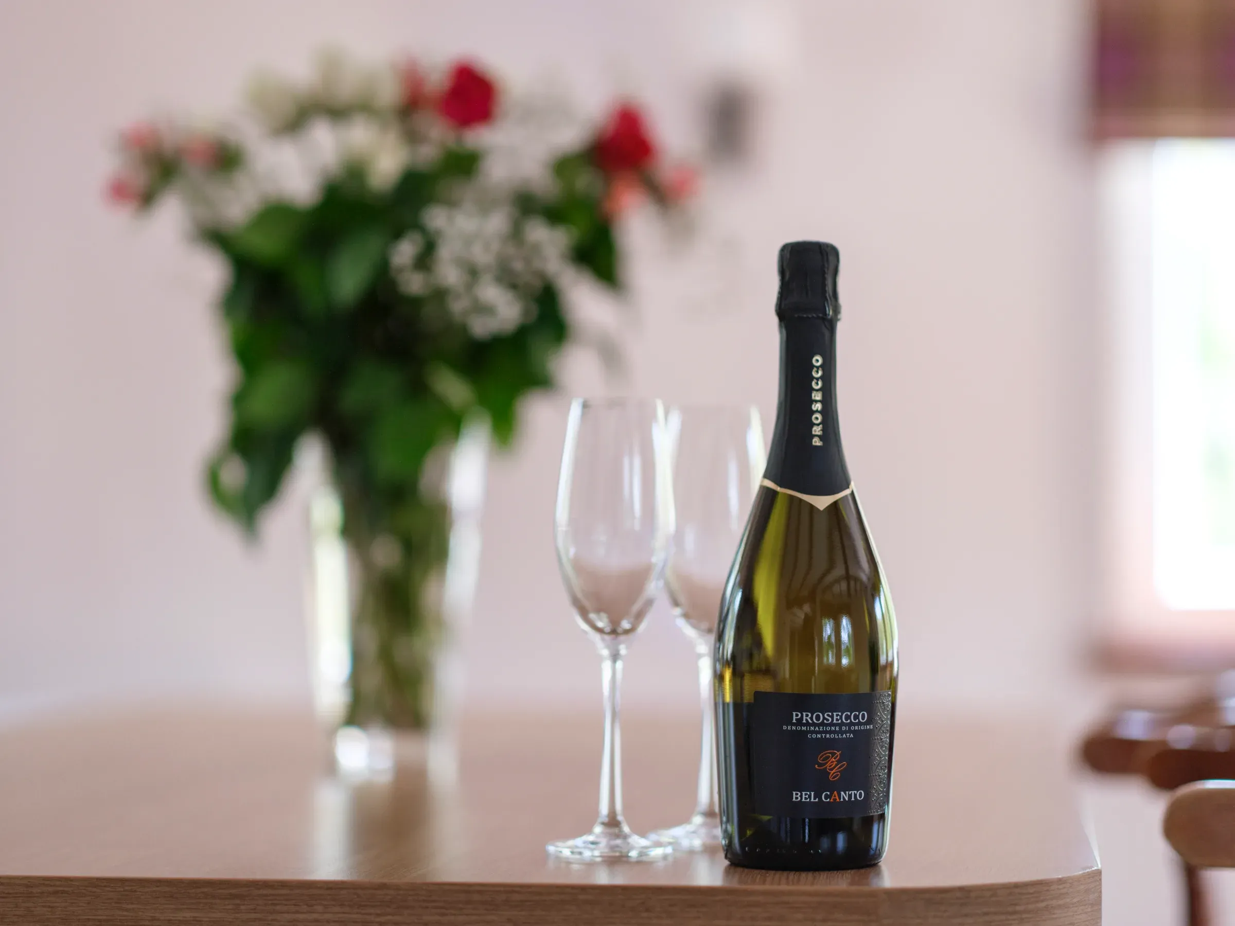 A bottle of prosecco and two empty glasses sit on a counter inside the lodge, accompanied by a floral arrangement.