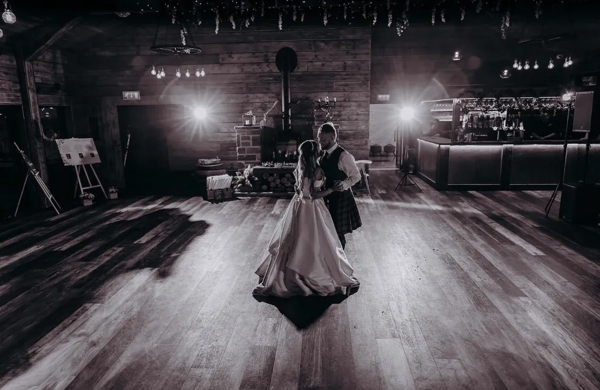 Claire and Callum's first dance in the Glen Clova wedding barn, wood-burning stove and fairy lights behind them